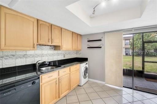 kitchen with dishwasher, a raised ceiling, washer / clothes dryer, decorative backsplash, and light brown cabinetry