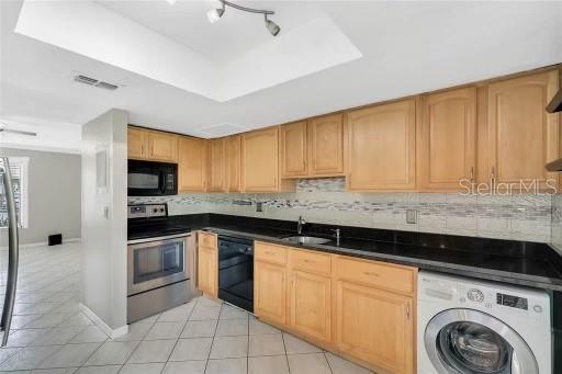 kitchen with sink, backsplash, washer / clothes dryer, light tile patterned flooring, and black appliances