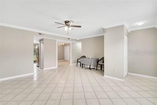 empty room featuring ceiling fan, light tile patterned flooring, and ornamental molding