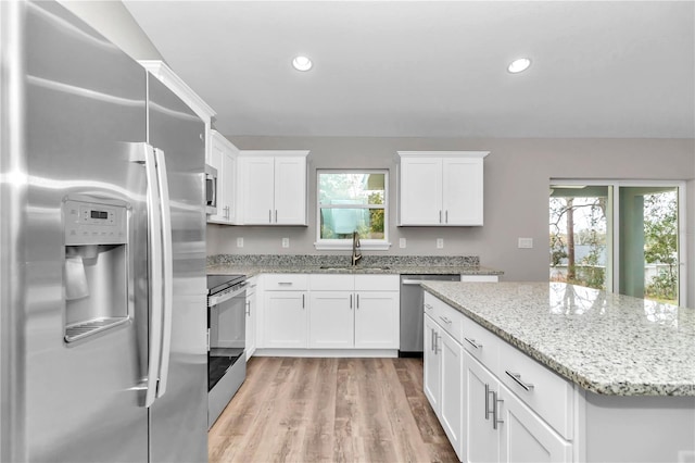 kitchen with light hardwood / wood-style floors, stainless steel appliances, light stone countertops, white cabinets, and sink