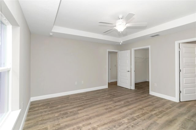 unfurnished bedroom with ceiling fan, wood-type flooring, a walk in closet, and a raised ceiling