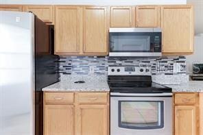 kitchen with light stone counters, stainless steel appliances, and light brown cabinetry