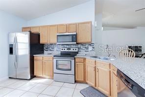 kitchen featuring tasteful backsplash, vaulted ceiling, light brown cabinetry, light tile patterned flooring, and appliances with stainless steel finishes