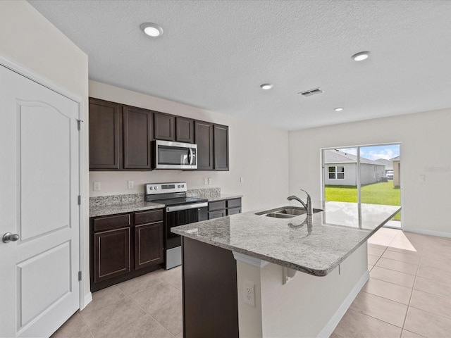 kitchen with light tile patterned floors, stainless steel appliances, a kitchen island with sink, and sink