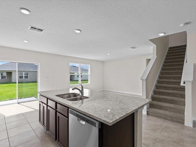 kitchen with dishwasher, a center island with sink, sink, light tile patterned flooring, and dark brown cabinetry