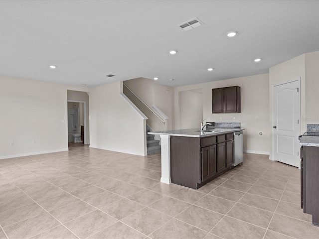 kitchen with dark brown cabinets, sink, light tile patterned floors, dishwasher, and an island with sink