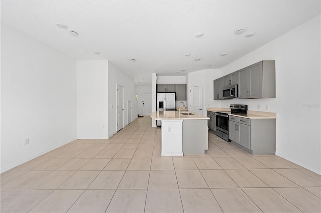 kitchen with gray cabinetry, sink, an island with sink, and appliances with stainless steel finishes