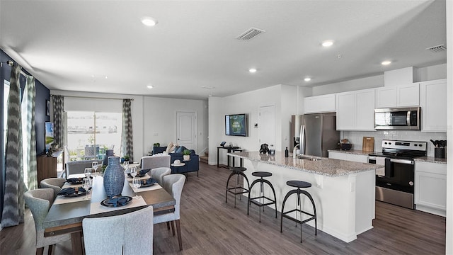 kitchen with a kitchen island with sink, dark wood-type flooring, white cabinets, light stone counters, and stainless steel appliances