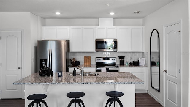 kitchen featuring appliances with stainless steel finishes, light stone counters, a kitchen island with sink, sink, and white cabinets