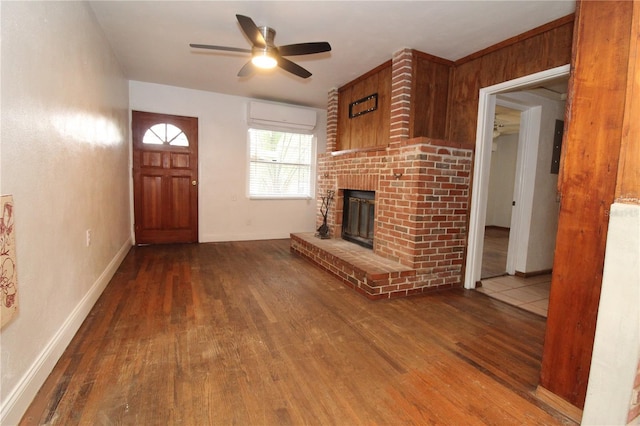 unfurnished living room featuring ceiling fan, a fireplace, wood finished floors, baseboards, and a wall mounted AC