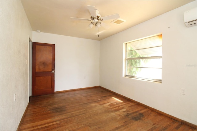 empty room featuring a wall unit AC, visible vents, ceiling fan, wood finished floors, and baseboards