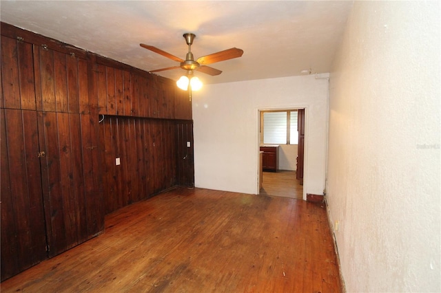 spare room featuring ceiling fan, wood walls, and wood finished floors