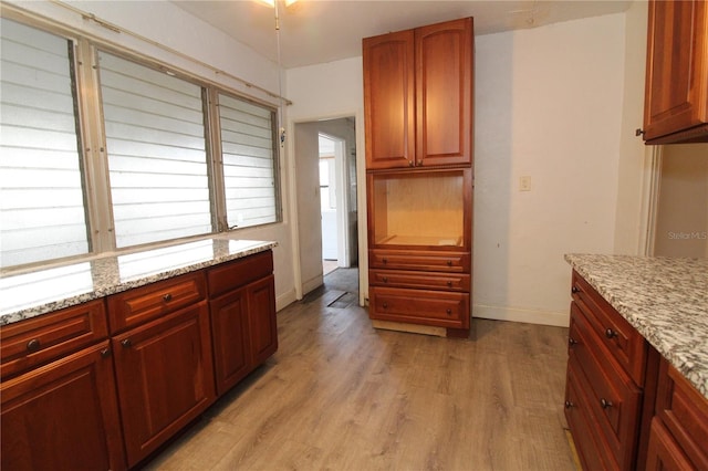 kitchen with baseboards, dark brown cabinets, light wood-type flooring, and light stone countertops