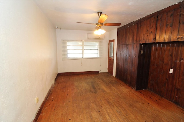 unfurnished bedroom featuring a wall mounted air conditioner, wood walls, a ceiling fan, a closet, and wood-type flooring