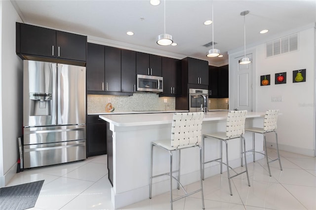 kitchen with appliances with stainless steel finishes, an island with sink, a kitchen bar, hanging light fixtures, and light tile patterned floors