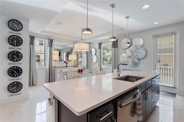 kitchen featuring sink, hanging light fixtures, an island with sink, stainless steel dishwasher, and a raised ceiling