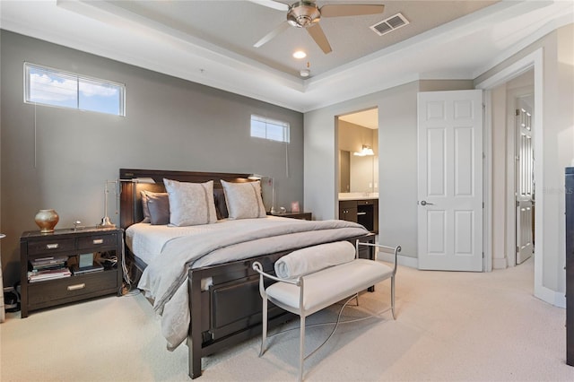 carpeted bedroom featuring ceiling fan, a tray ceiling, and ensuite bath