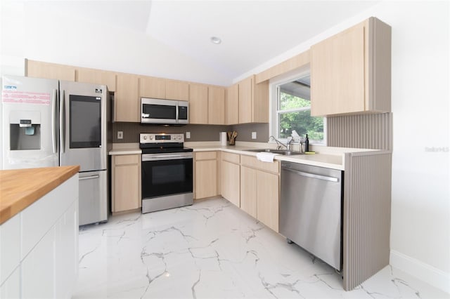 kitchen with light brown cabinetry, sink, stainless steel appliances, and vaulted ceiling