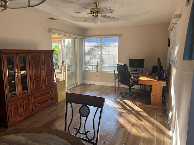 office featuring a textured ceiling, ceiling fan, a tray ceiling, and dark hardwood / wood-style floors