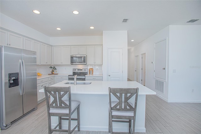 kitchen featuring a kitchen bar, a center island with sink, light wood-type flooring, and appliances with stainless steel finishes