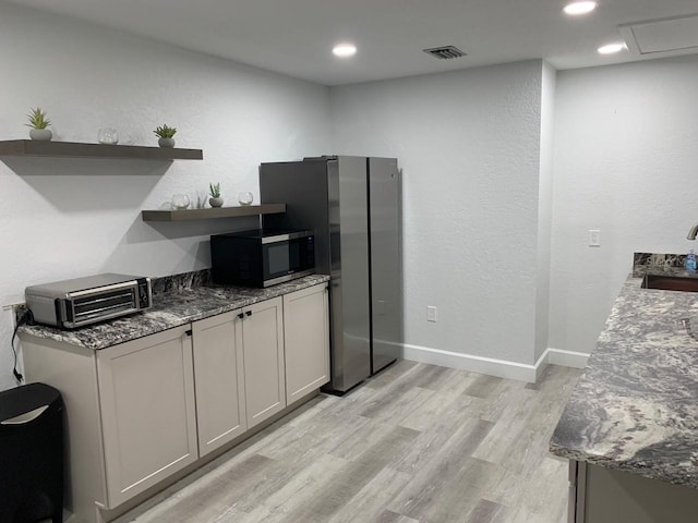 kitchen with gray cabinetry, light hardwood / wood-style floors, dark stone counters, and sink