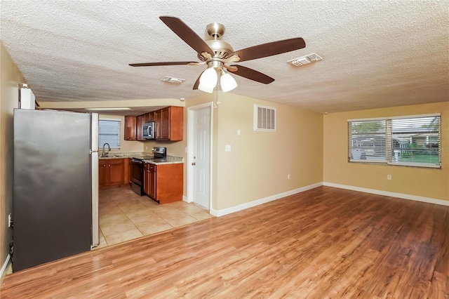 kitchen with ceiling fan, sink, light hardwood / wood-style floors, a textured ceiling, and appliances with stainless steel finishes