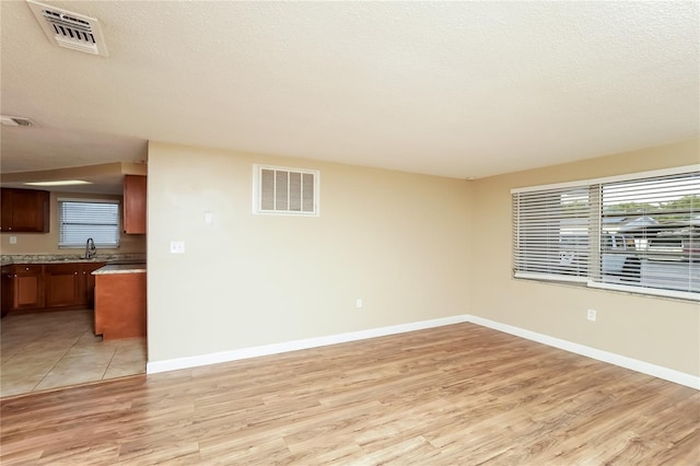 unfurnished room featuring a textured ceiling, light wood-type flooring, and sink