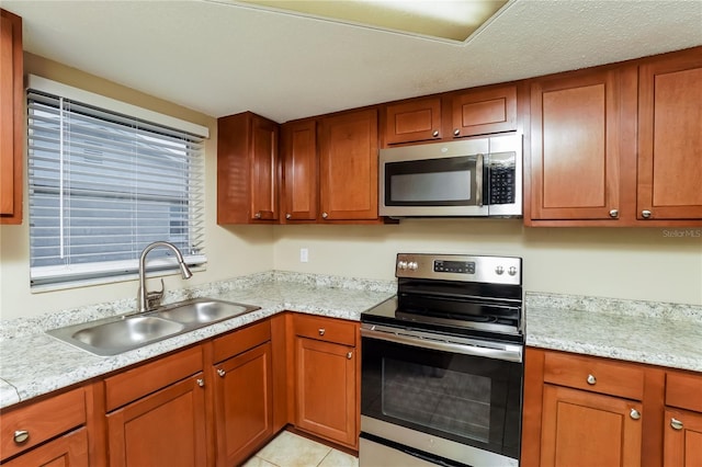 kitchen with appliances with stainless steel finishes, light stone counters, light tile patterned floors, and sink