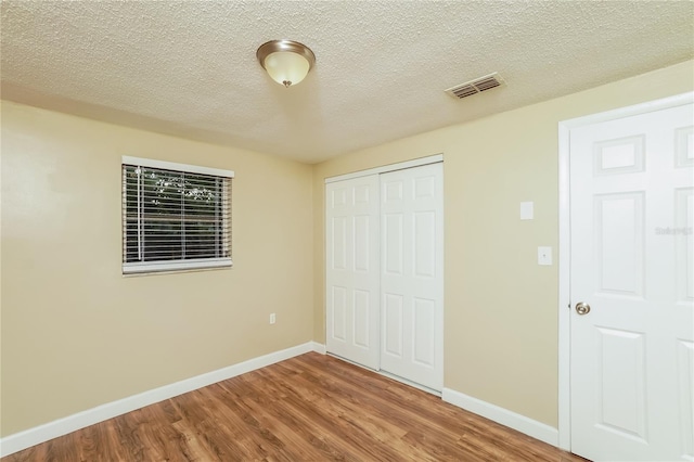 unfurnished bedroom with a textured ceiling, hardwood / wood-style flooring, and a closet