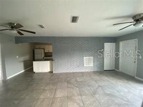 unfurnished living room featuring wallpapered walls, a ceiling fan, baseboards, and an accent wall