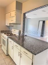 kitchen featuring light tile patterned floors, dark stone counters, and white gas range oven