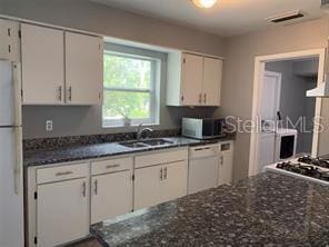 kitchen featuring white cabinetry, white appliances, visible vents, and a sink