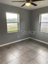 tiled empty room featuring baseboards and a ceiling fan