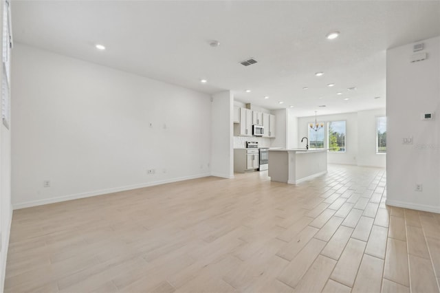 unfurnished living room with sink, a chandelier, and light wood-type flooring