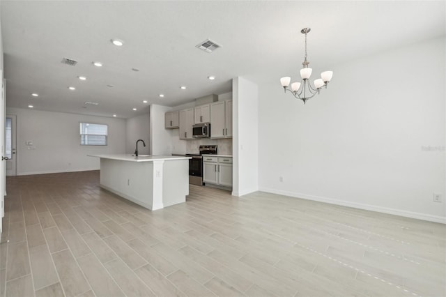 kitchen with appliances with stainless steel finishes, pendant lighting, gray cabinetry, light hardwood / wood-style floors, and a center island with sink