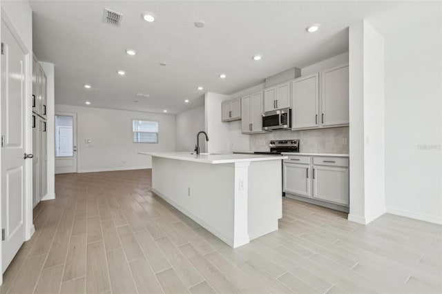 kitchen featuring a kitchen island with sink, sink, light wood-type flooring, and appliances with stainless steel finishes