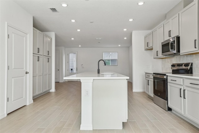 kitchen featuring white cabinetry, appliances with stainless steel finishes, an island with sink, and decorative backsplash