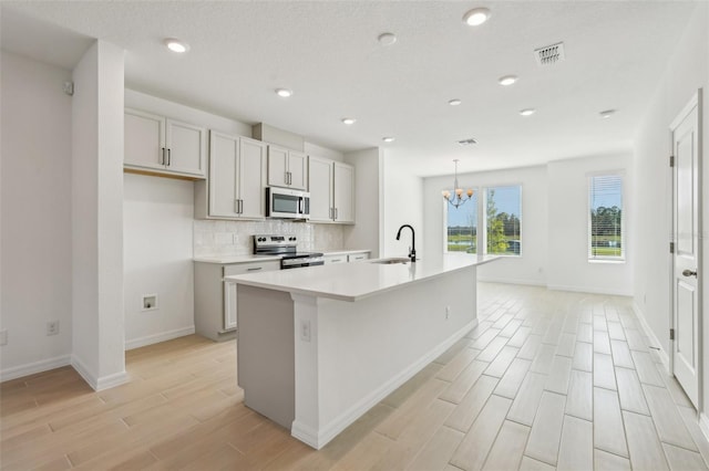 kitchen featuring decorative light fixtures, sink, stainless steel appliances, a center island with sink, and light hardwood / wood-style flooring