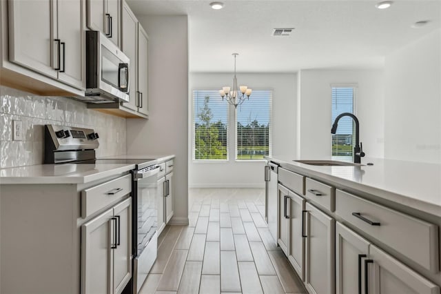 kitchen featuring sink, a chandelier, decorative backsplash, hanging light fixtures, and stainless steel appliances