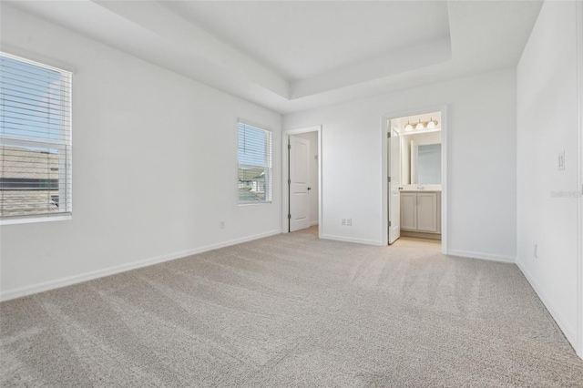 unfurnished bedroom featuring a raised ceiling, light carpet, and ensuite bath