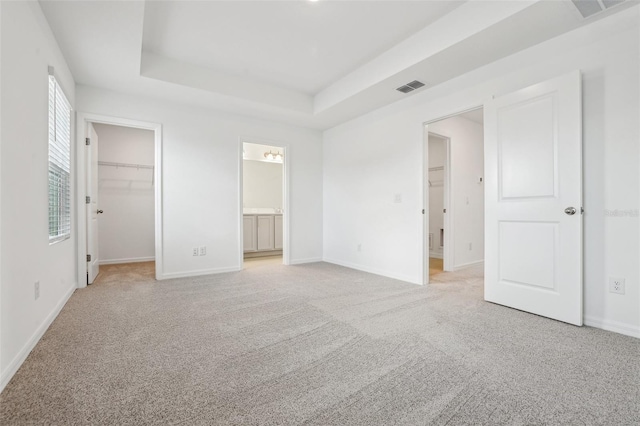 unfurnished bedroom featuring a walk in closet, ensuite bath, light carpet, a tray ceiling, and a closet