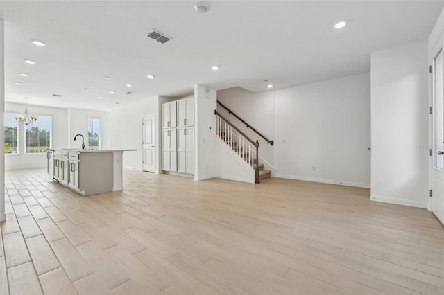 interior space with sink, an inviting chandelier, hanging light fixtures, light hardwood / wood-style floors, and an island with sink