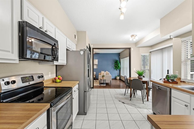 kitchen with wood counters, white cabinets, light tile patterned floors, and appliances with stainless steel finishes