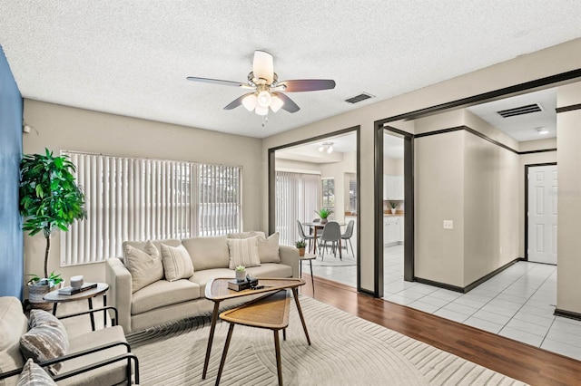 living room with ceiling fan, a textured ceiling, and light wood-type flooring