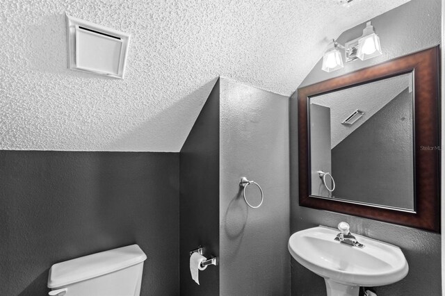 bathroom featuring a textured ceiling, toilet, lofted ceiling, and sink