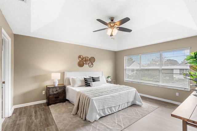 bedroom with ceiling fan, a raised ceiling, and light wood-type flooring