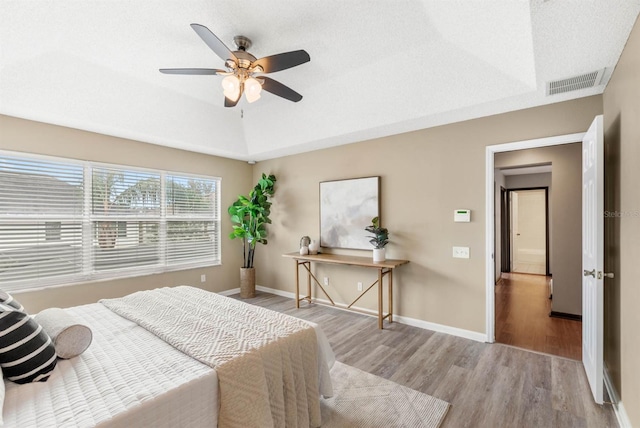 bedroom with light hardwood / wood-style flooring, a raised ceiling, and ceiling fan