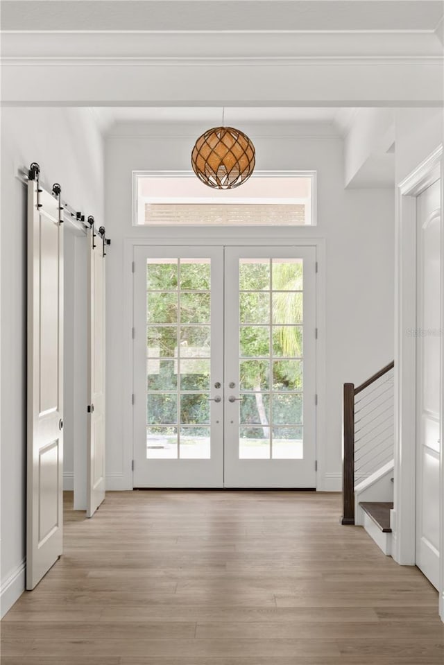 doorway to outside with crown molding, a barn door, light wood-type flooring, and french doors