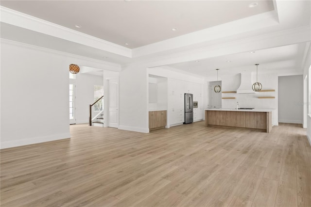 unfurnished living room with a raised ceiling, ornamental molding, and light hardwood / wood-style flooring