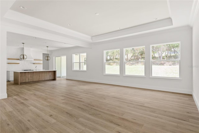 unfurnished living room with a healthy amount of sunlight, a tray ceiling, and light hardwood / wood-style floors